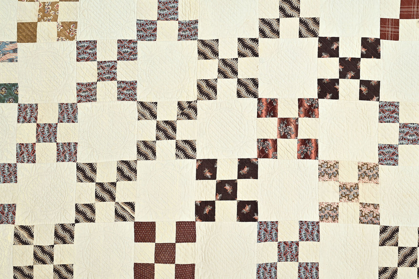 Close up view of Chintz Nine Patch quilt showing small square quilt patches of varying patterns against a cream colored background. 